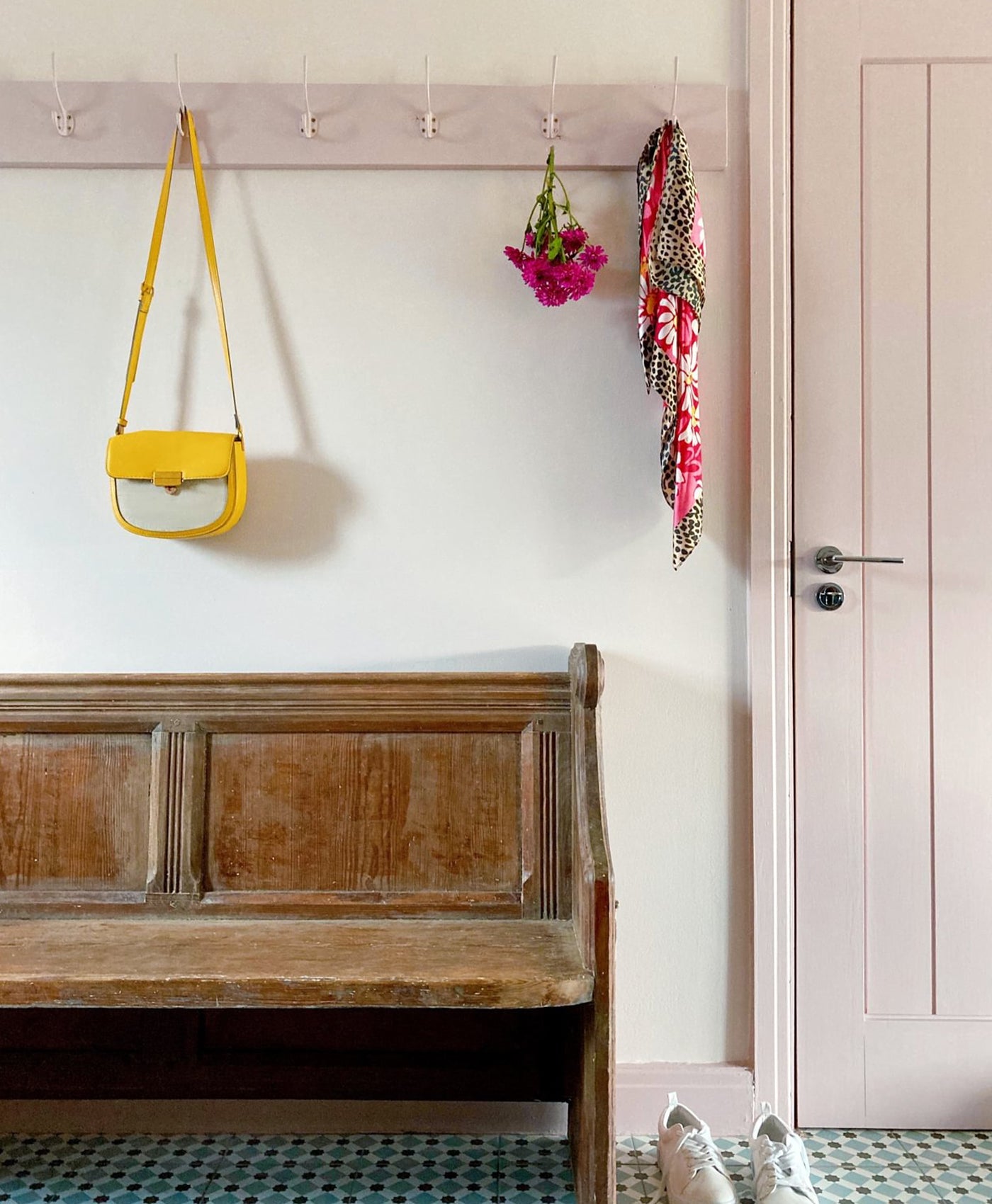 Wooden bench with a yellow bag and floral decorations hanging on hooks against a white wall with pale pink trims