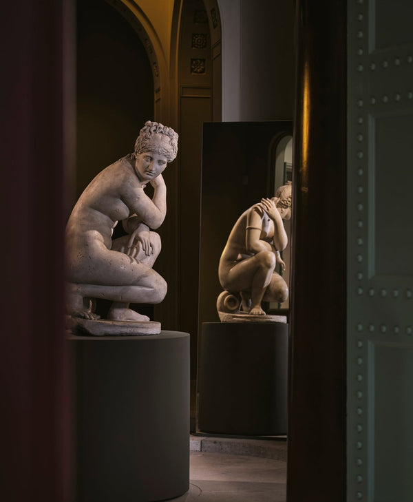 Statue of a思考的人物 in a museum setting with a mirror reflecting the statue.