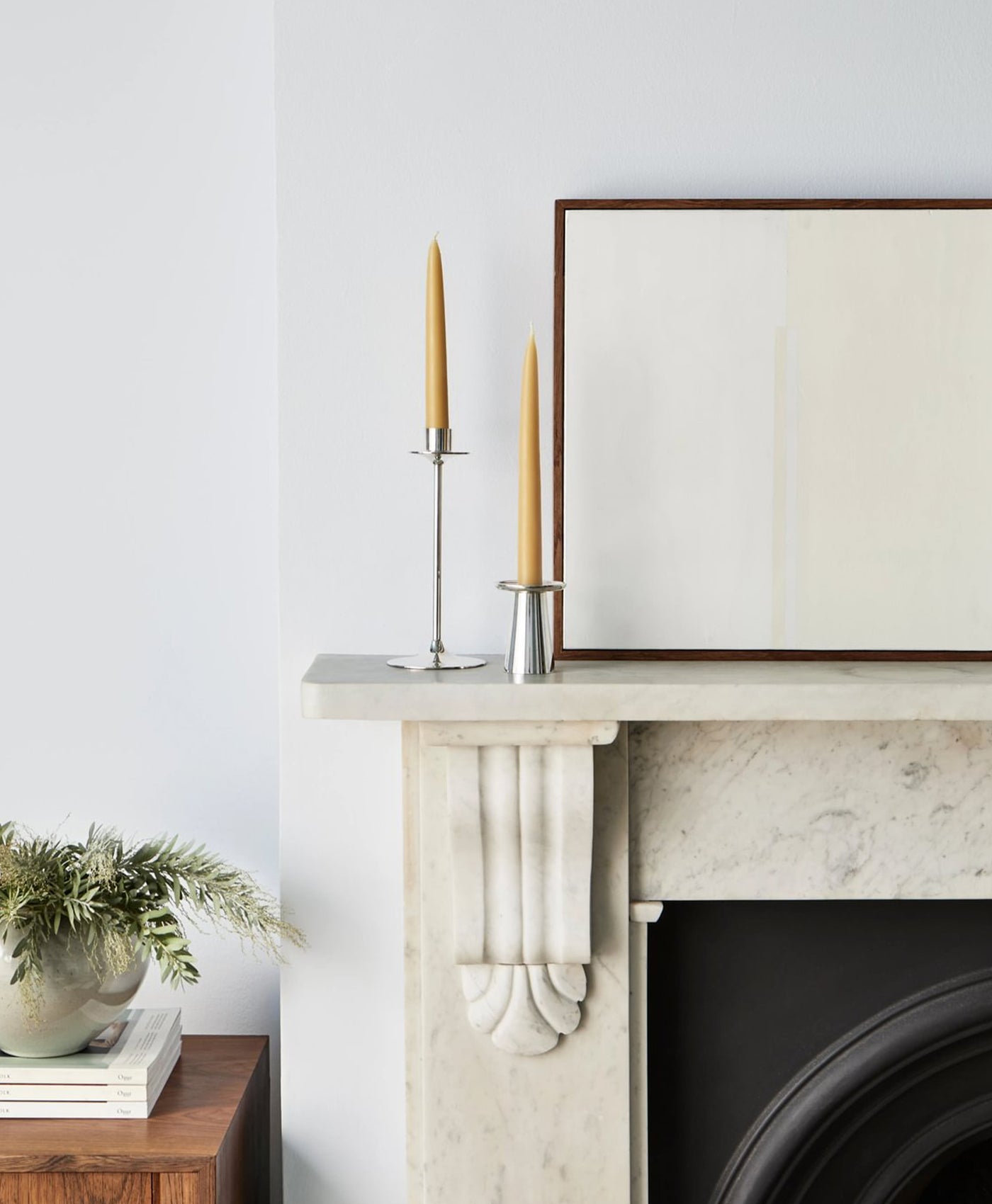 Decorative setup on a fireplace mantle with candles and a framed picture walls painted in cool white paint