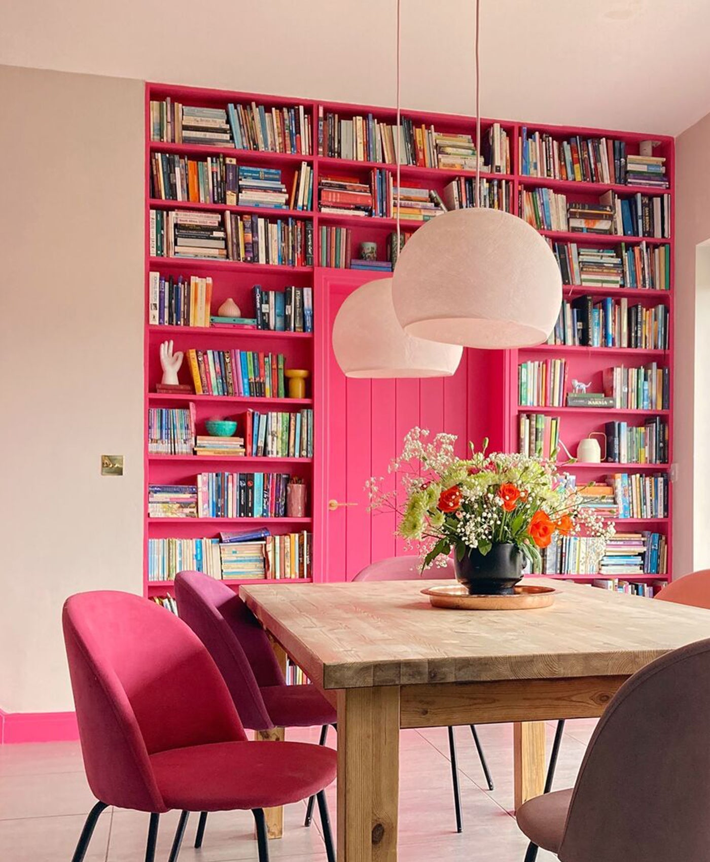 Dining area with pink built-in bookshelves, shocking pink chairs, and a wooden table.