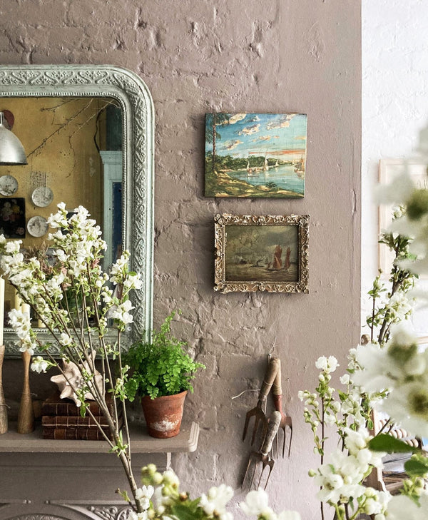 Decorative mocha brown wall with a mirror, paintings, and plants in a home setting.