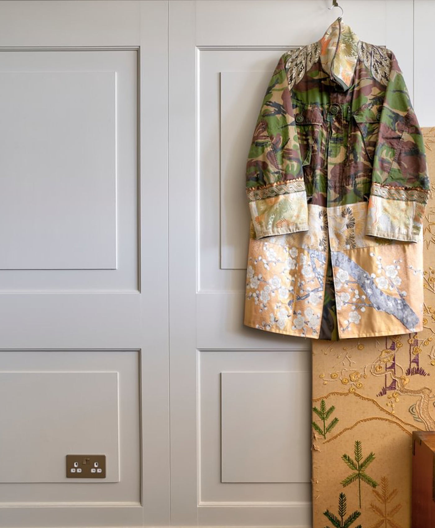 Camouflage-patterned jacket hanging on a hook against a white paneled wall.