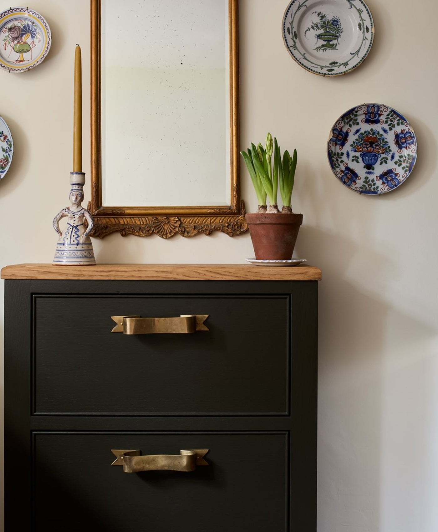 brown Black dresser with gold handles, mirror, and decorative plates on a warm white wall.