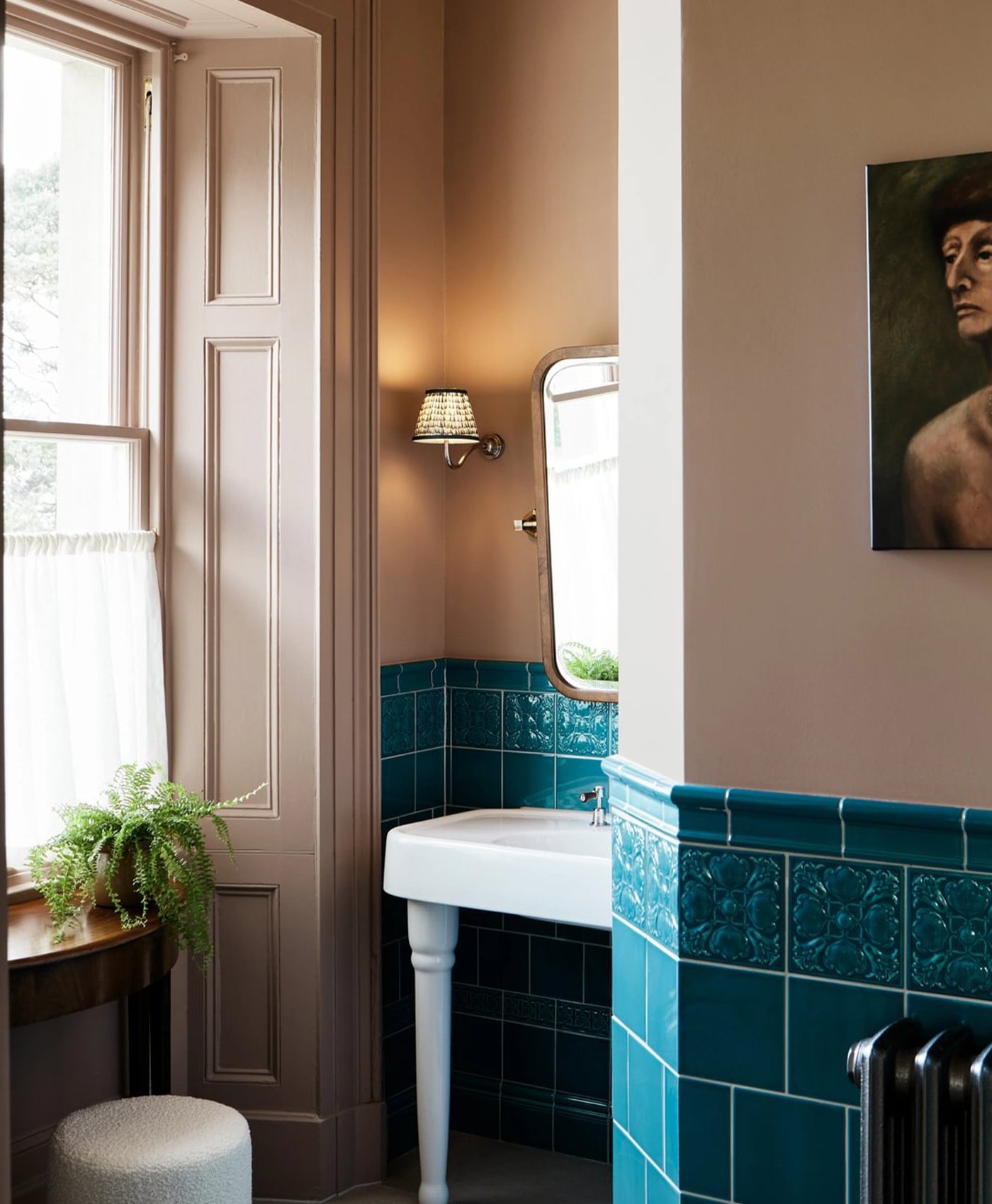 Plaster pink bathroom with teal tiles, white sink, and a painting on the wall.