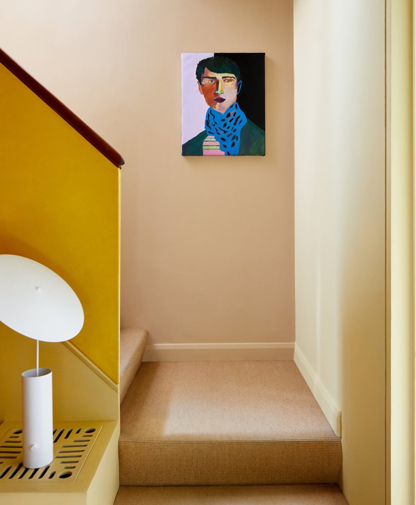 Staircase with one yellow wall and one neutral painted wall, white lamp, and a painting of a man on the wall.