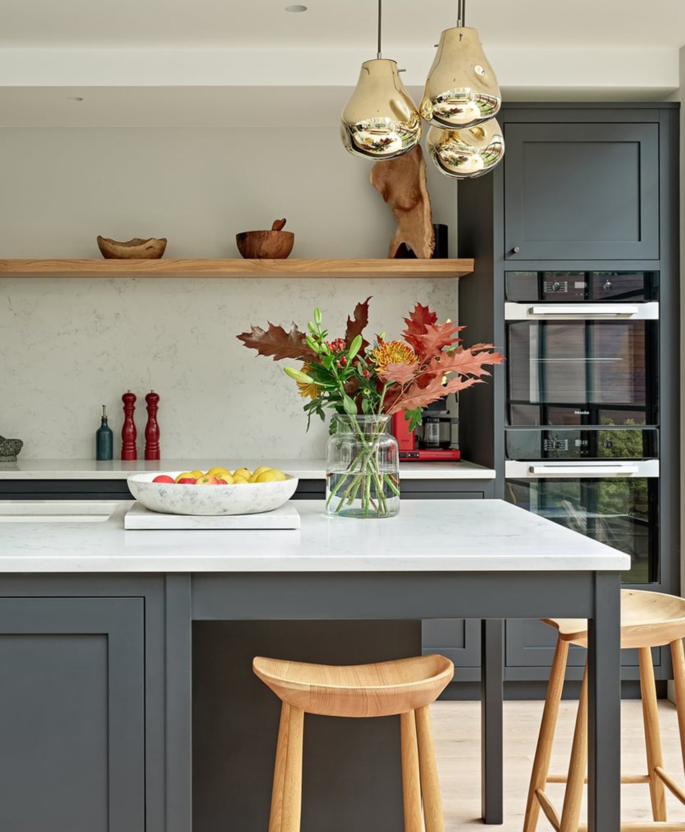Modern kitchen with charcoal painting cabinets, a central island, wooden stools, and decorative elements.