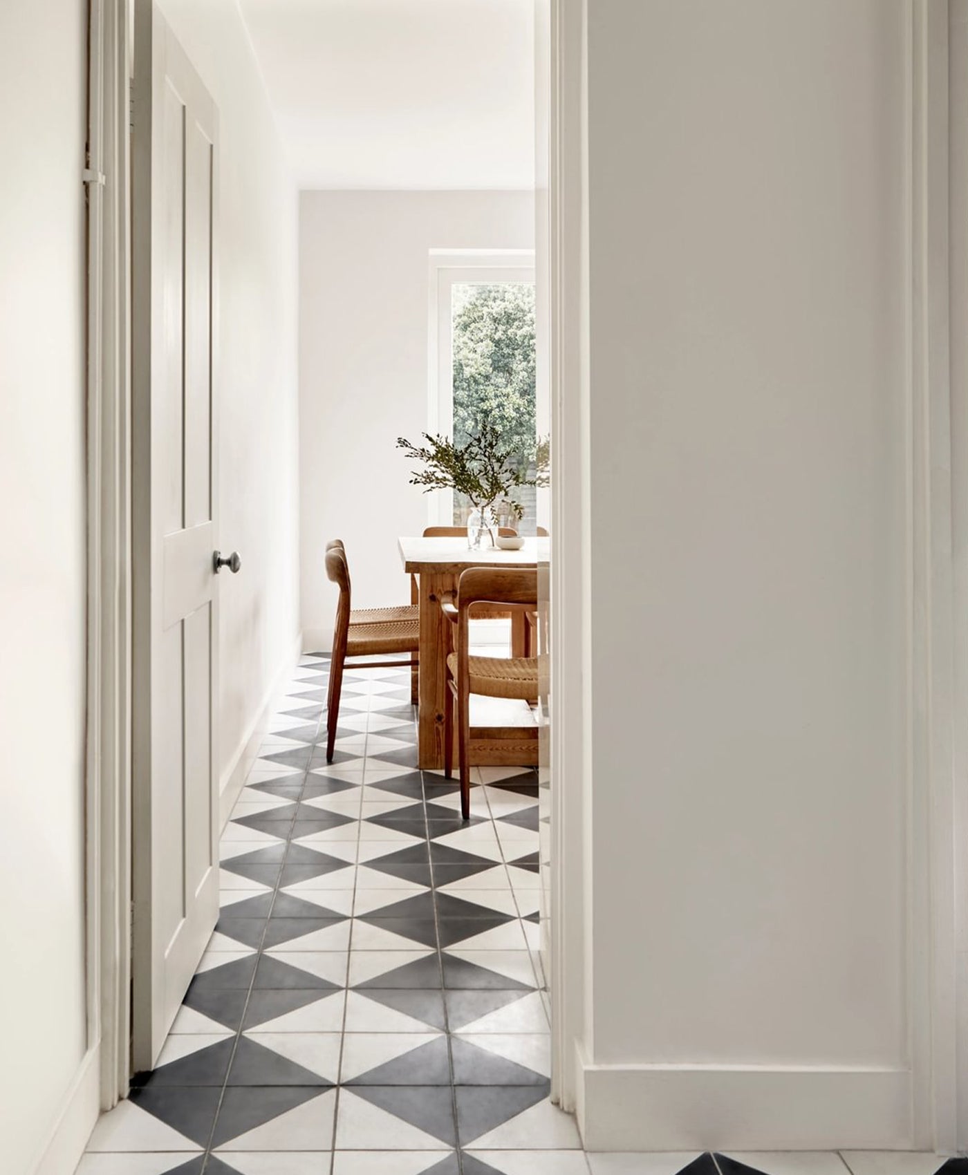 White Dining room with wooden table and chairs, black and white tiled floor, and white walls.