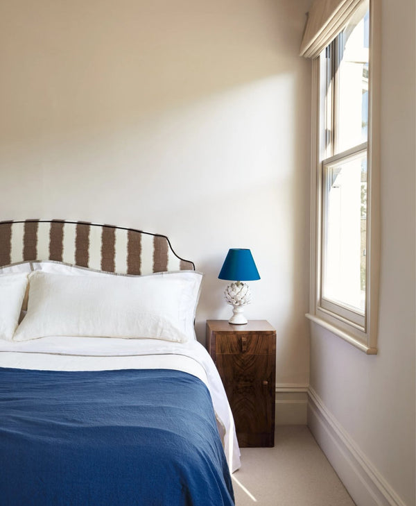 Warm off-white bedroom with striped headboard, blue bedding, and a lamp on a nightstand.