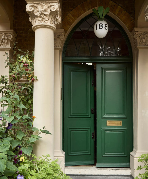 Green exterior door with decorative number '188' above it, flanked by columns and plants.