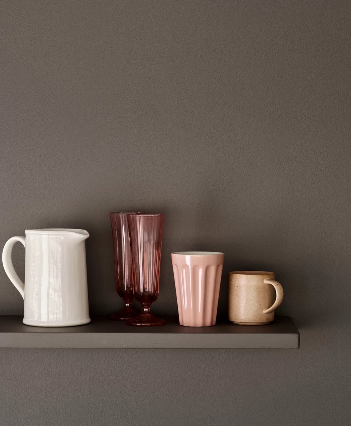 Set of ceramic mugs and a pitcher on a mocha grey shelf against a matching background