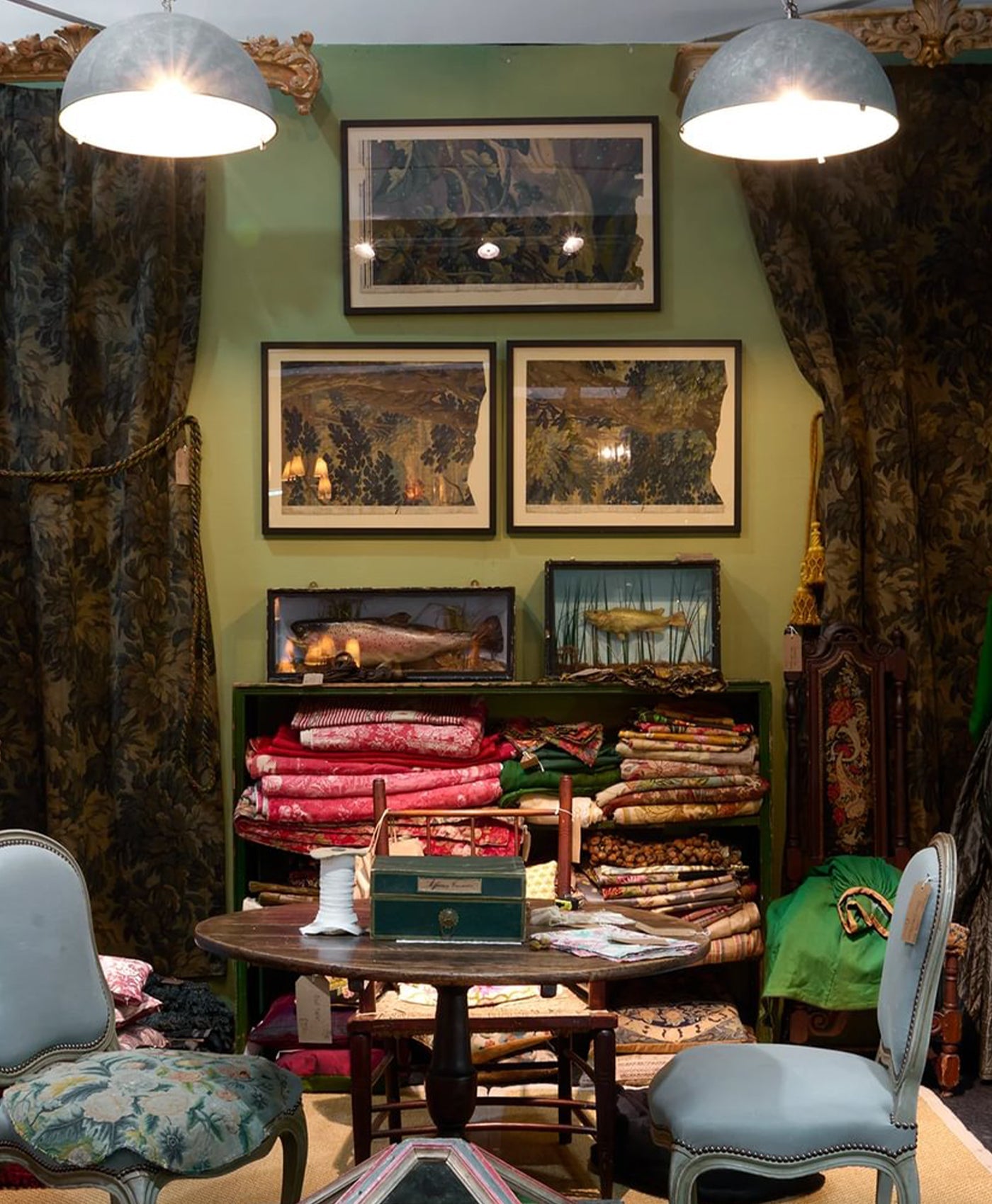 Room with green walls, framed pictures, and a table with fabric samples.