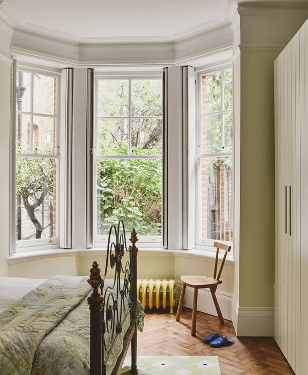 Bedroom in pale yellow green colour with bay window, radiator, and wooden chair