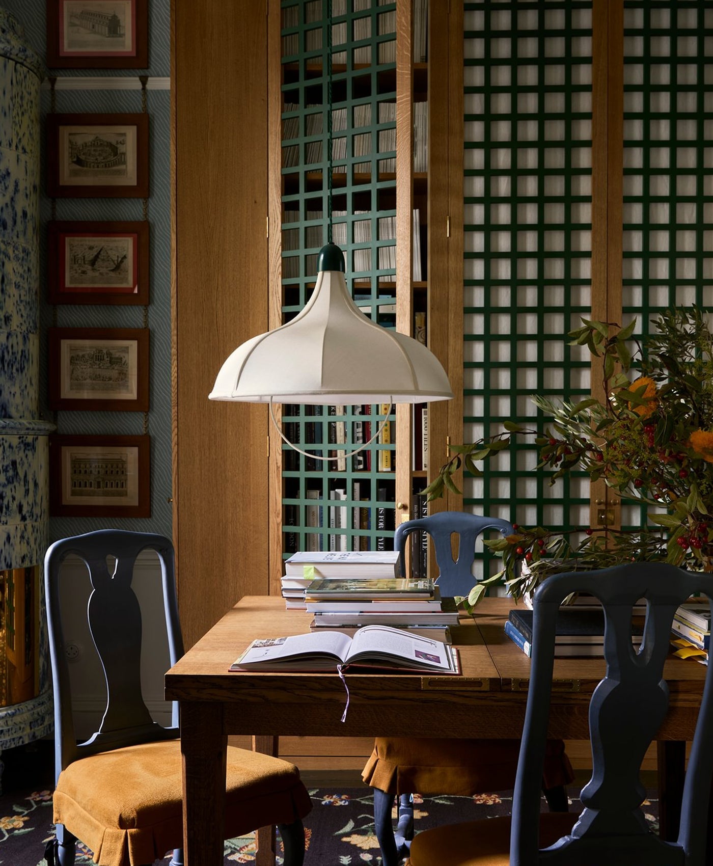 Dining area with wooden table, navy blue painted chairs, and a lamp in a room with decorative green lattice detail on the walls.