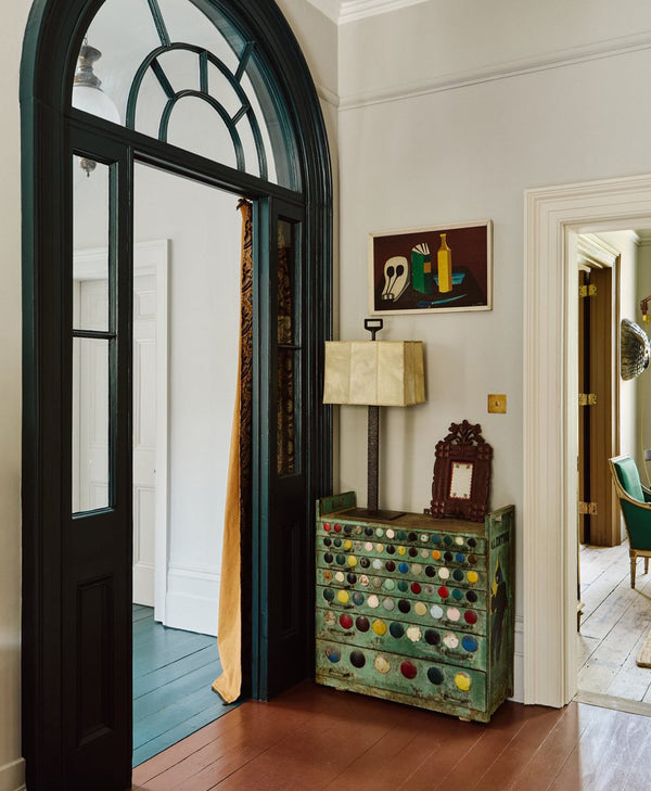Pale grey interior of a room with a dark green door frame, decorative cabinet and lamp.
