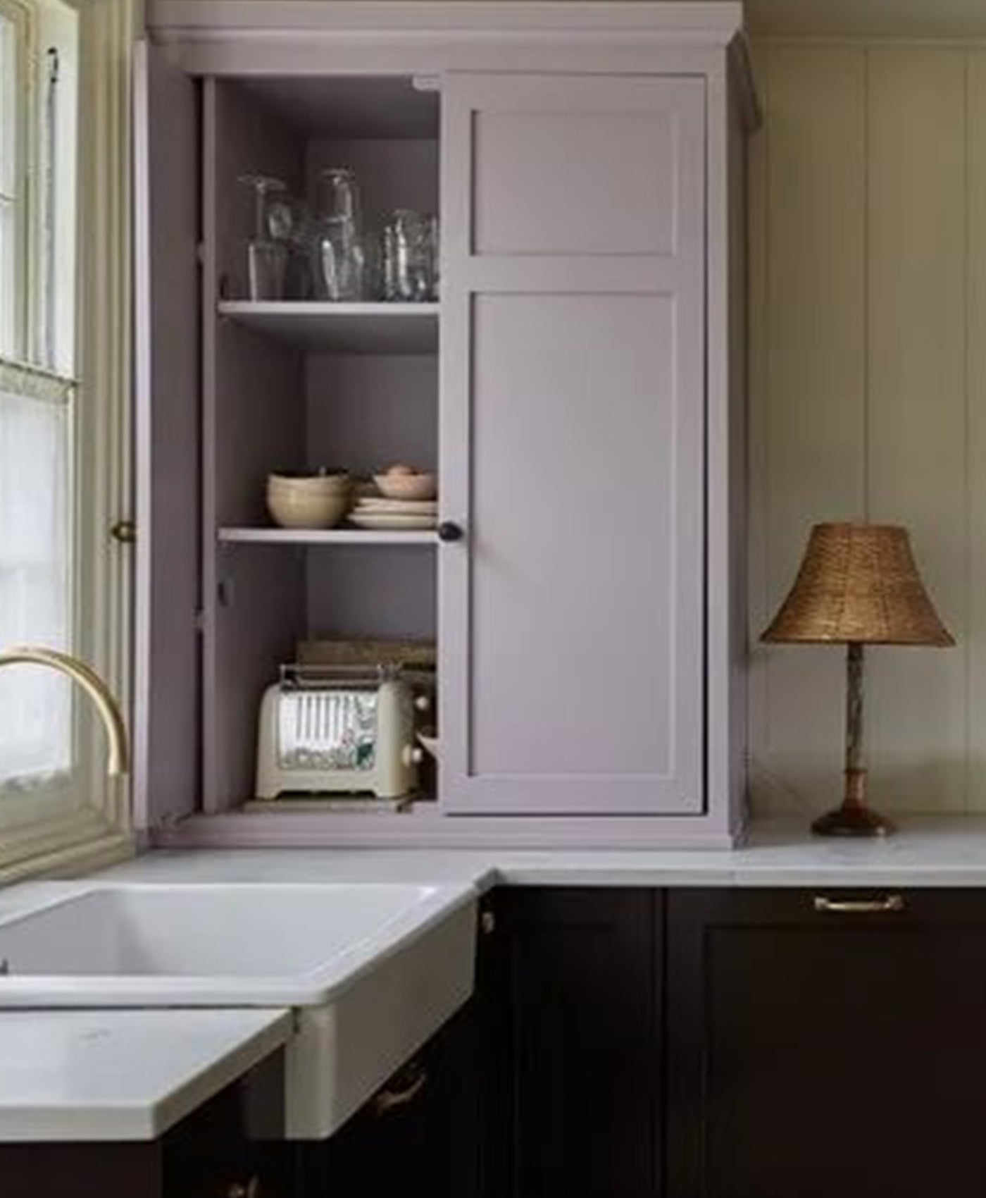 Kitchen interior with lilac and dark brown painted cabinets, sink, and lamp.
