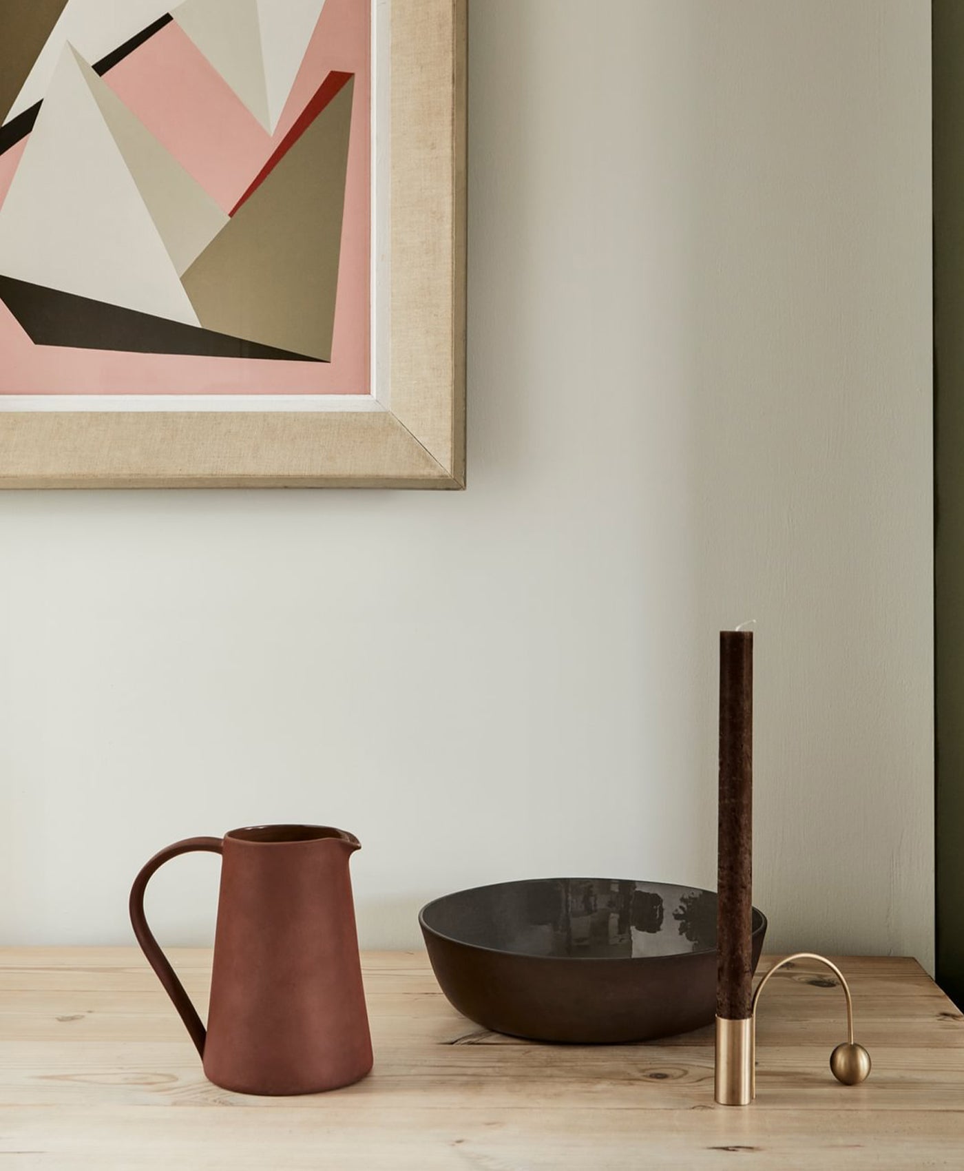 Decorative items including a pitcher, bowl, and tall vase on a wooden surface with abstract art in the background.
