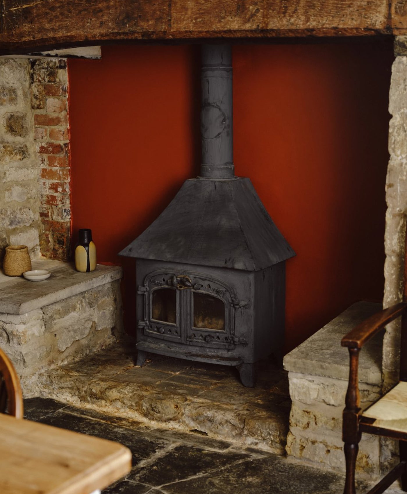 Traditional stone fireplace with a black cast iron stove against a red wall.
