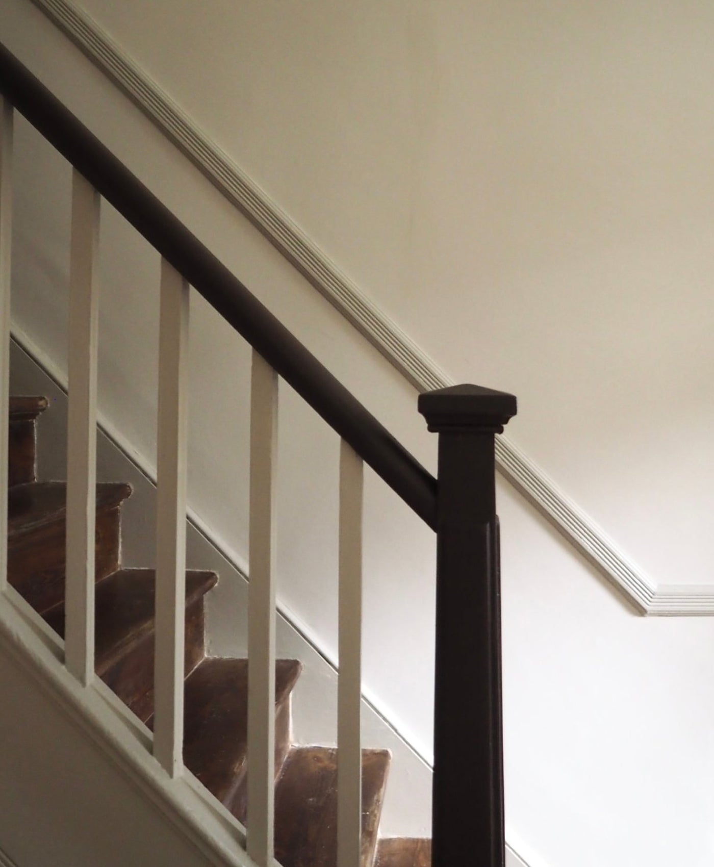 Staircase with wooden steps and a dark brown handrail against a warm neutral wall.