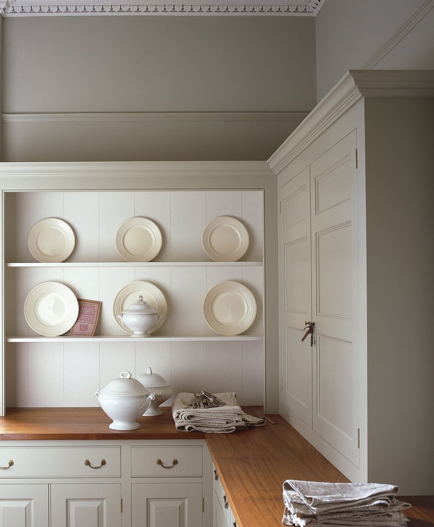 Stone coloured kitchen with neutral white shelves displaying plates and a wooden countertop.