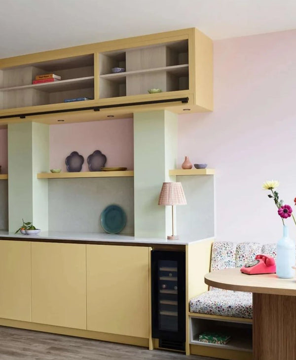 Retro kitchen with wooden cabinets in pastel shades including pale yellow, mint green, pastel pink, shelves, and a small table.