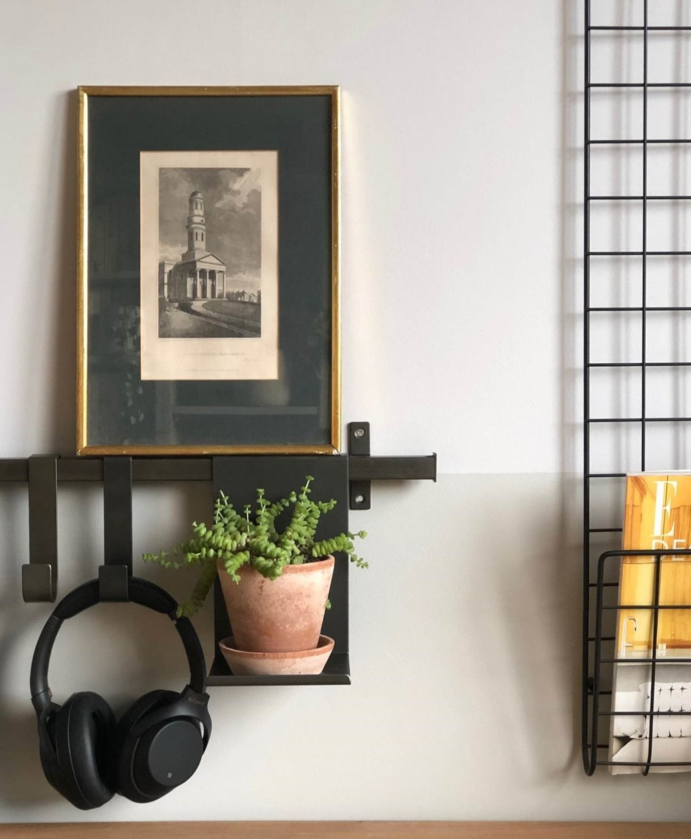 Wall-mounted shelf with headphones, plant, and framed picture mounted on a pale wall
