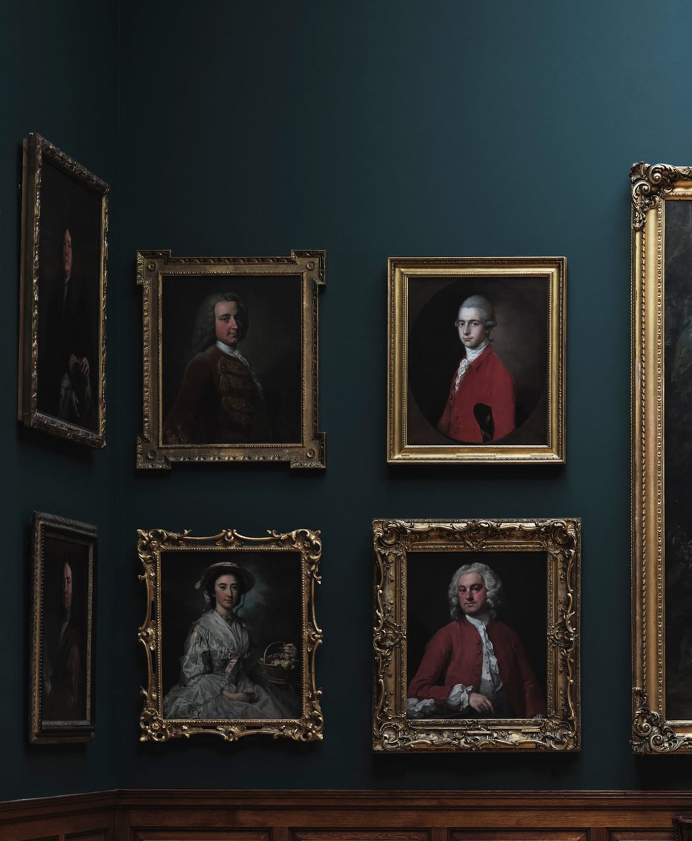 Collection of classical portraits in ornate frames on a dark green wall.