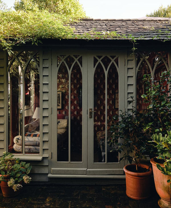 Garden shed painted in sage green with decorative arched windows and potted plants