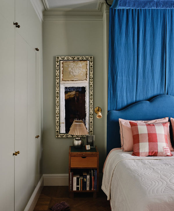 Mint green bedroom with blue headboard, plaid pillow, and decorative mirror.