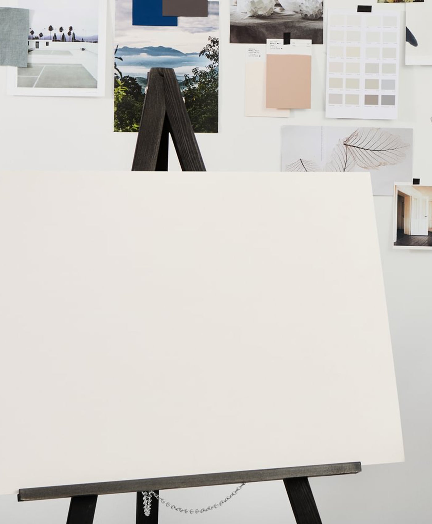 White canvas on an easel with a wall of art prints and color swatches in the background
