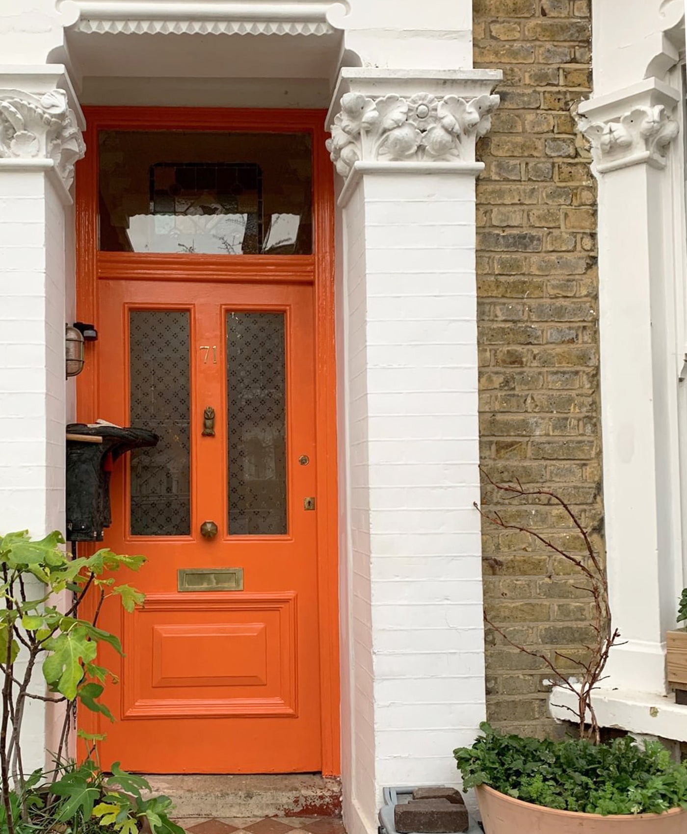 Bright orange front door of a house with white walls and brick accents.