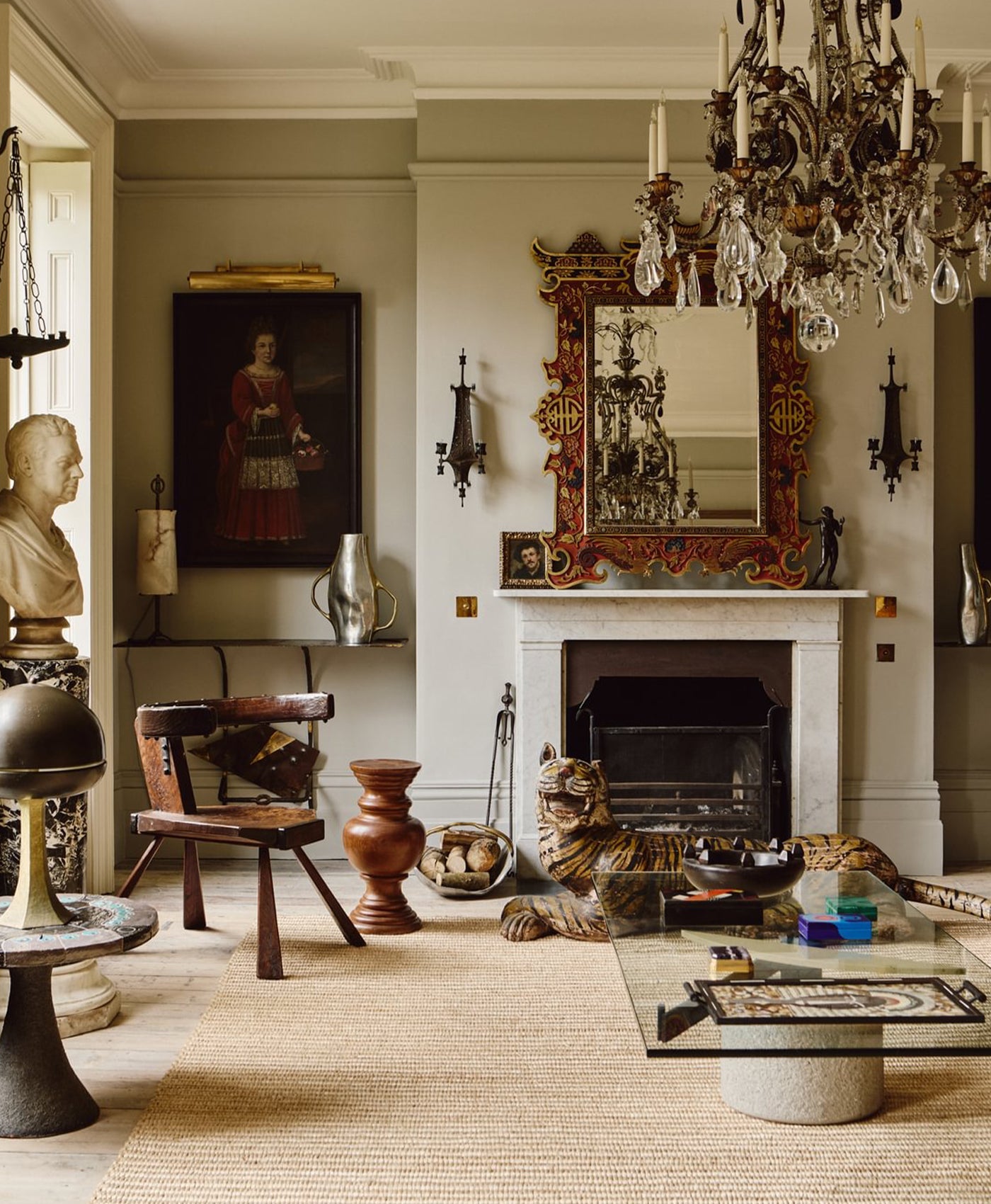 Warm grey living room with classical decor, including a chandelier, fireplace, and various sculptures.