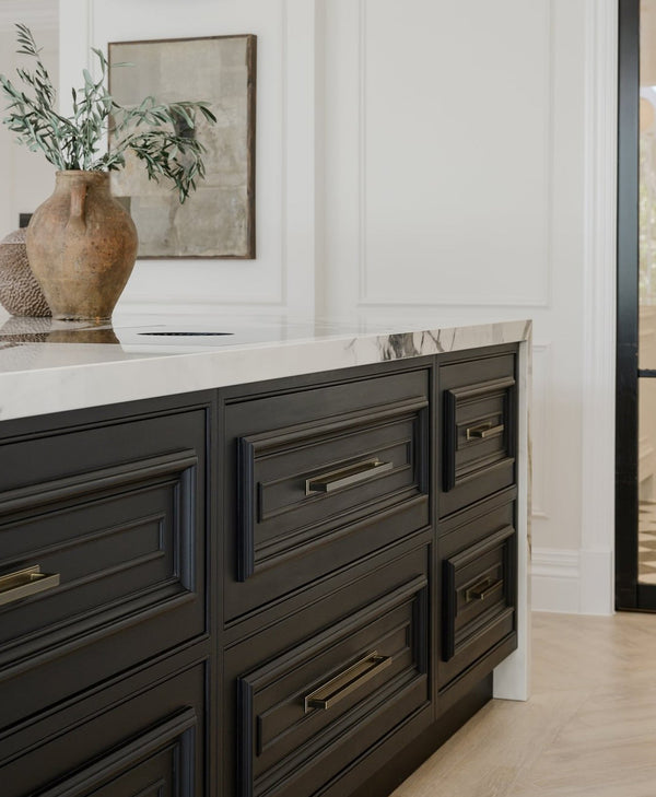 Black kitchen island with marble countertop and decorative items in a room with white walls and a painting.