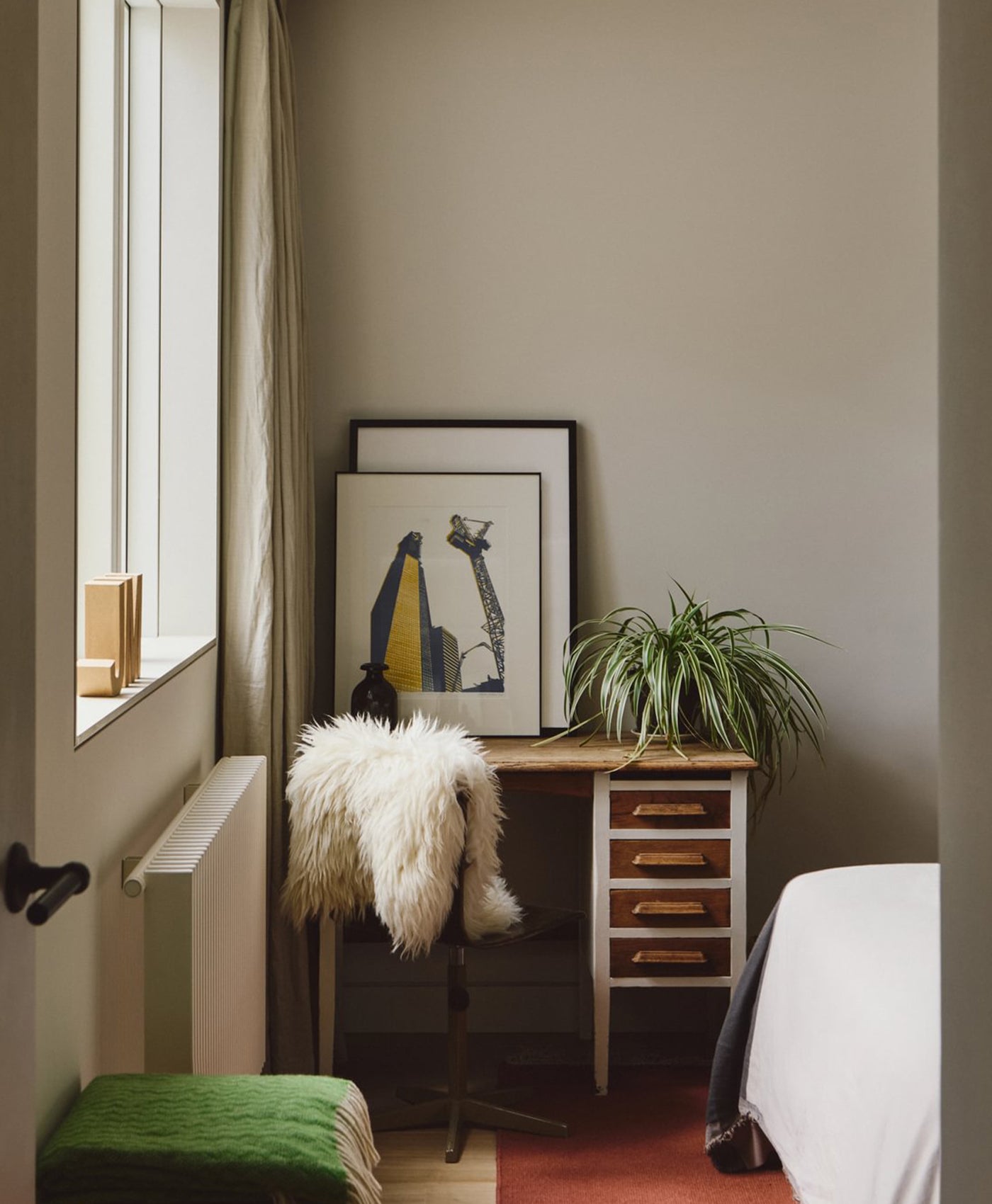 Small bedroom in light neutral colour with a desk, chair, and decorative items.
