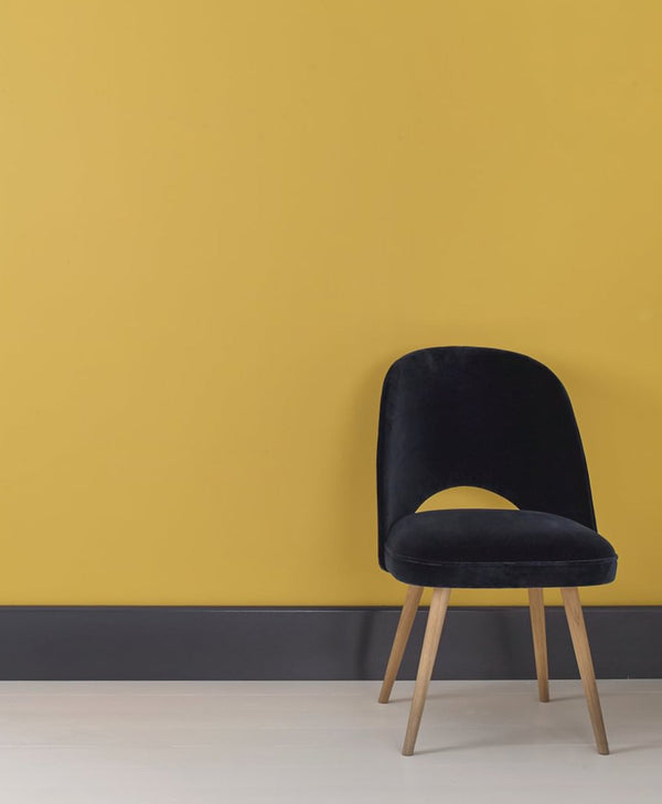 Black chair with wooden legs against a mustard yellow wall, with black skirting and a white floor