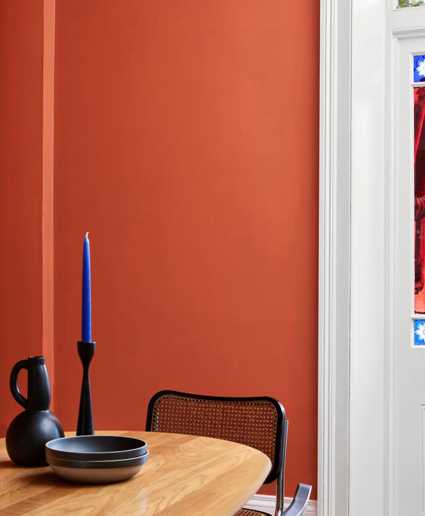 Orange dining area with a wooden table, black chairs, and a blue candle