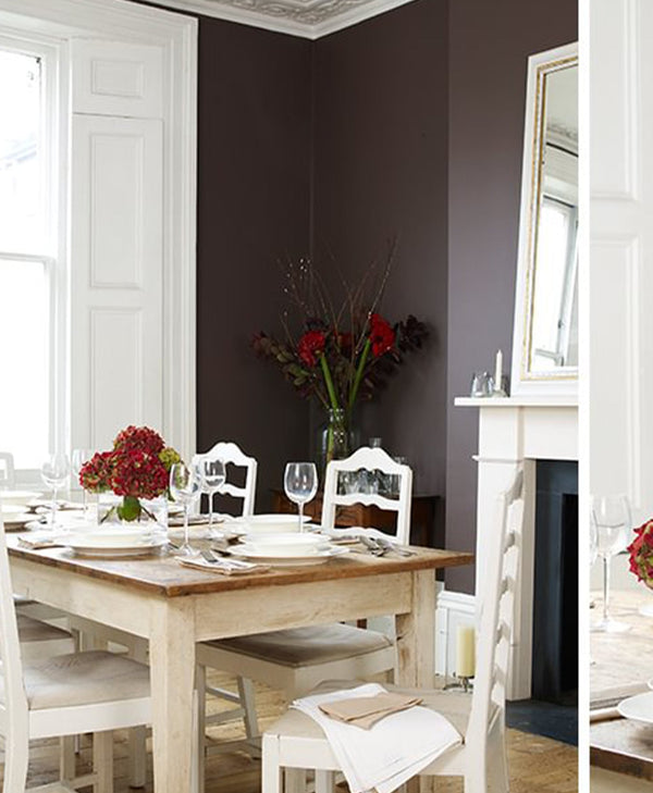 Dining room with a wooden table set for a meal, white chairs, and dark plum coloured walls.