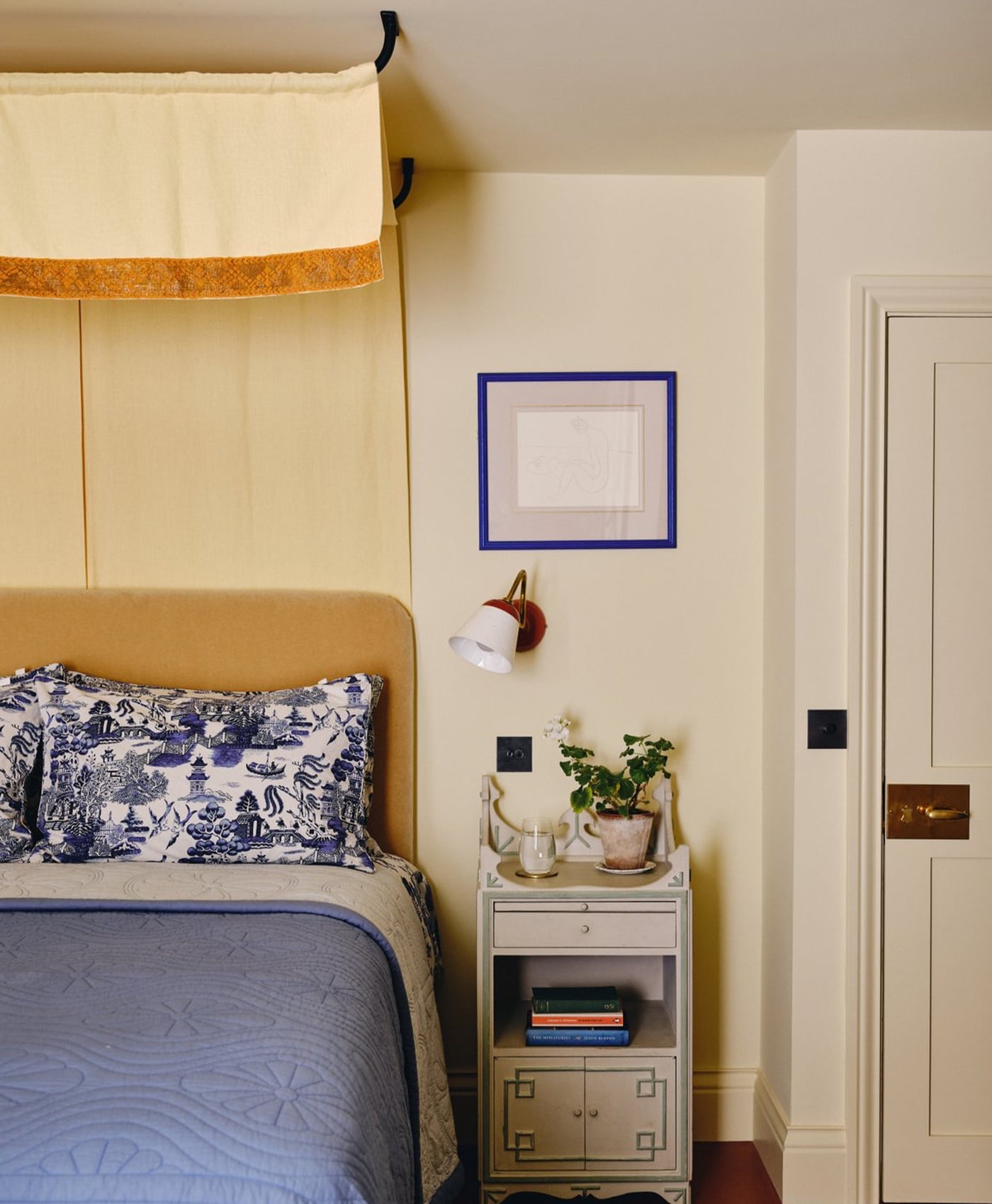 Butter bedroom with beige headboard, blue and white pillows, and a nightstand with decor items.