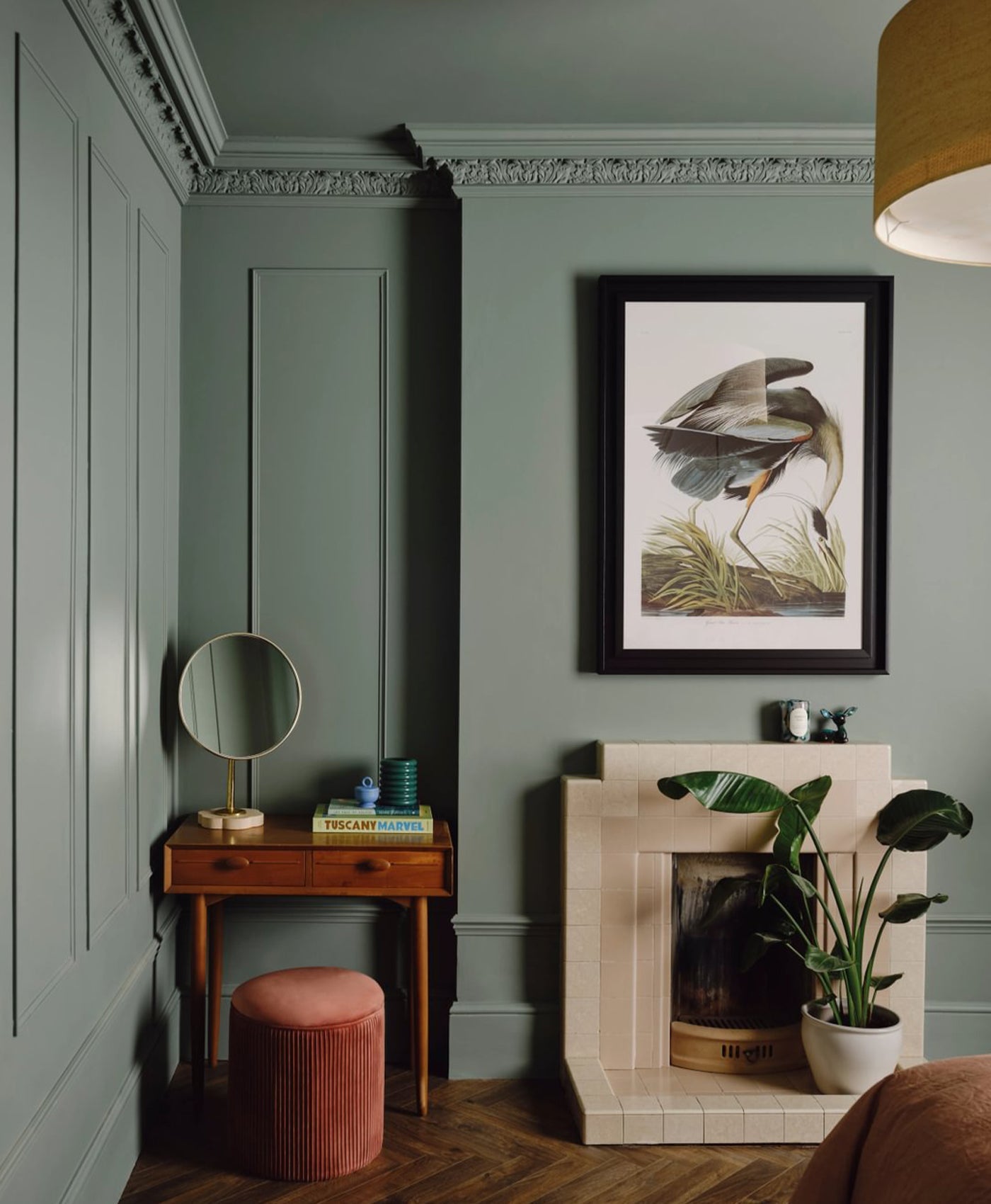 colour drenched sage green room interior with a fireplace, framed artwork, and small table.