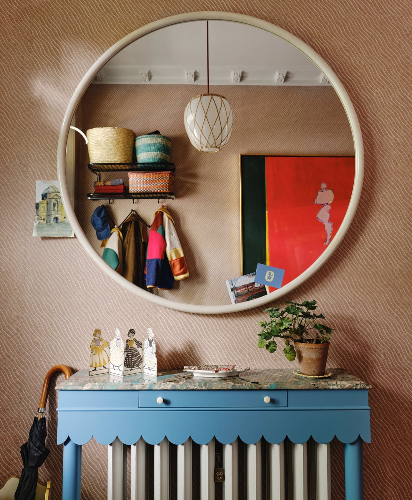 Round mirror on a wall with a blue cabinet below, featuring decorative items.