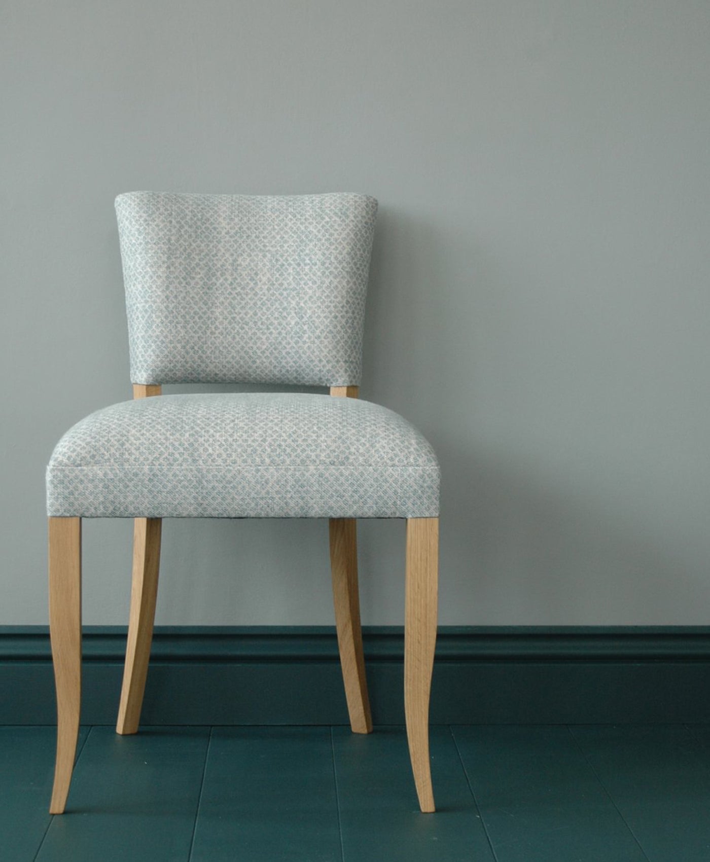 Chair with patterned grey cushion and wooden legs against a blue grey wall.