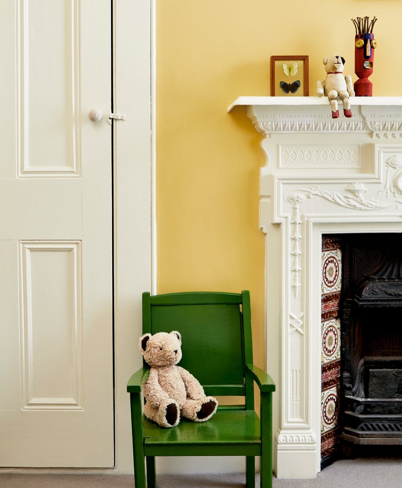 Green chair with a teddy bear in front of a pale yellow green fireplace in a sunshine yellow room