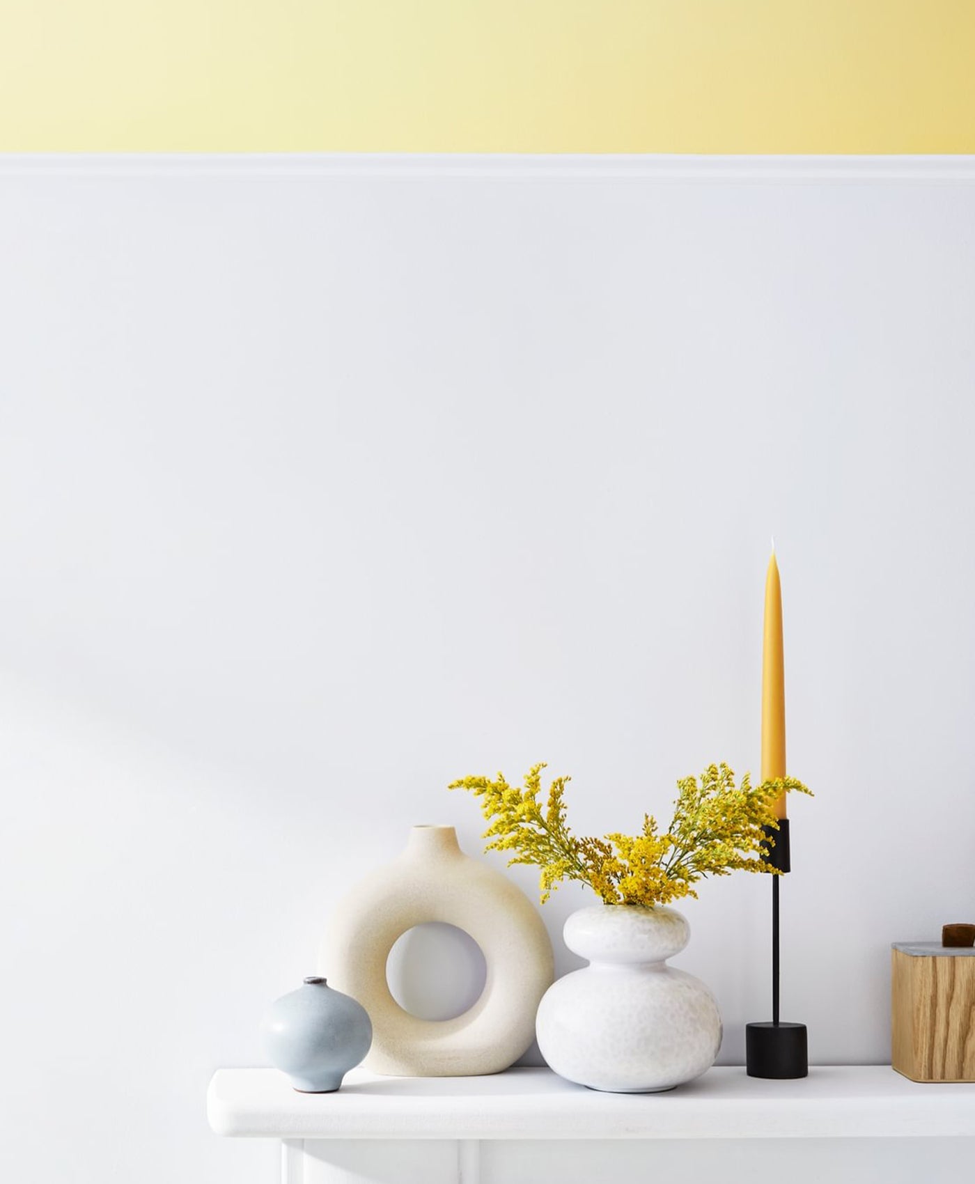 Decorative setup with vases, a candle, and plants on a white surface against a light gray wall.