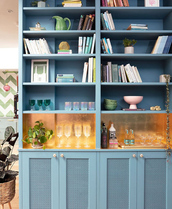 Mid =blue bookshelf with various items including books, glasses, and bottles.