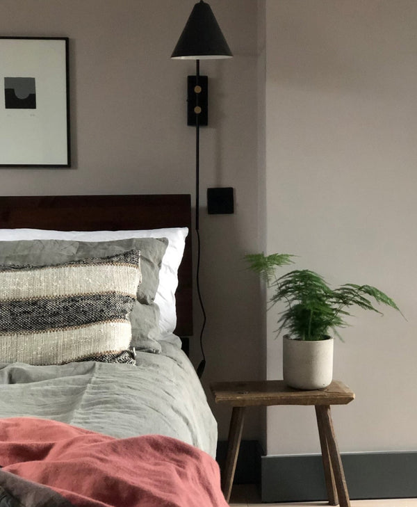 warm grey bedroom with bed, side table, and wall lamp and black skirting