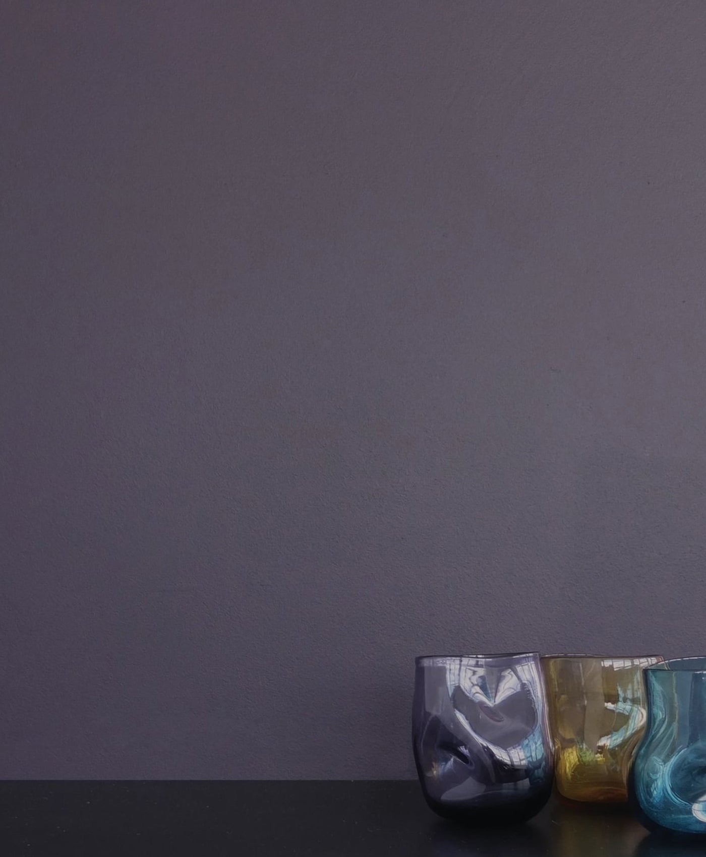 Three glass tumblers in blue, green, and gold on a dark surface with a deep purple background