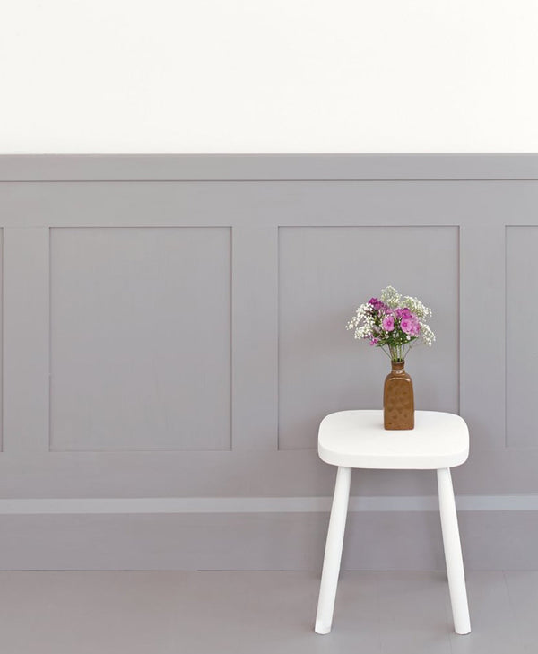 White stool with a vase of flowers against a grey panelled wall