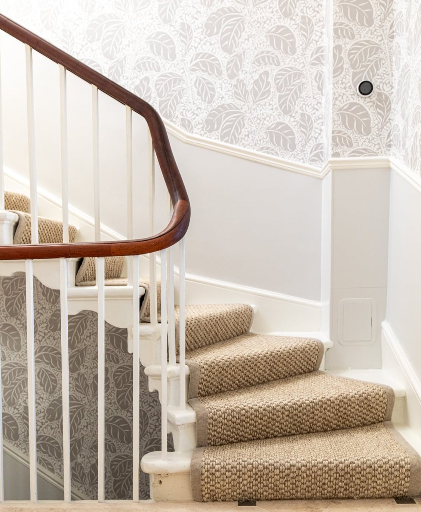 Staircase with stair runner and wooden handrail against a decorative wall.