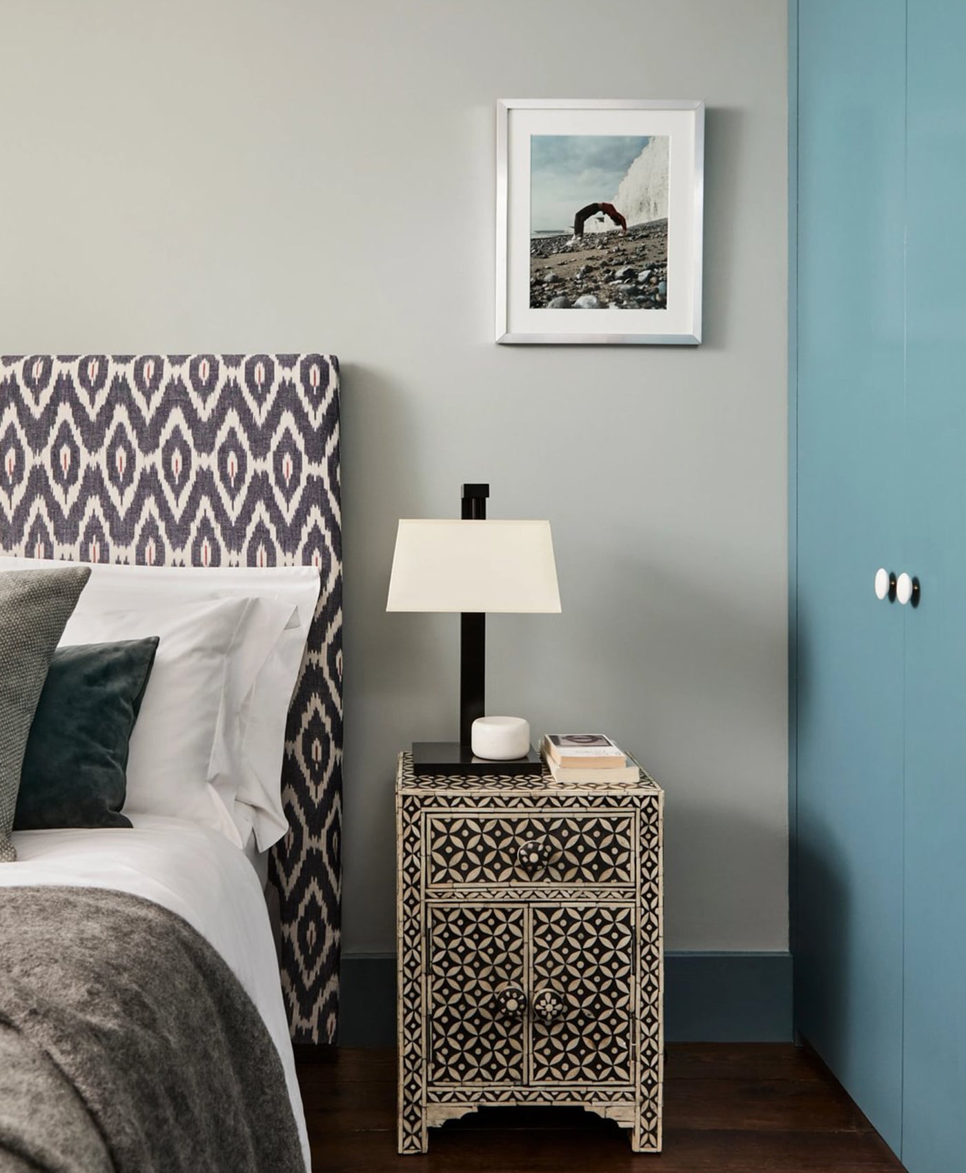 Mint green bedroom with patterned headboard, nightstand, and framed picture on wall.