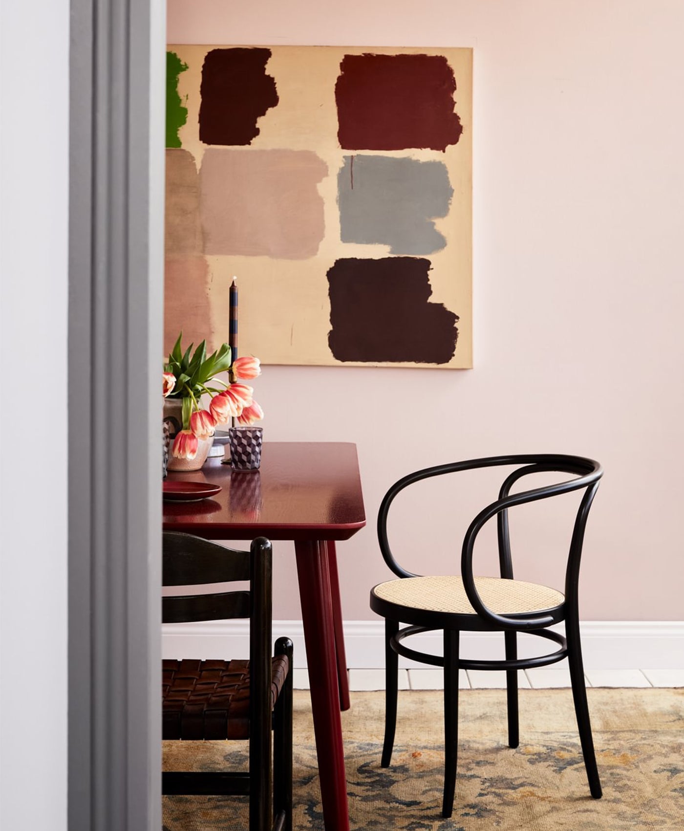 dusty pink Dining room with a red table and black chairs, abstract painting on the wall.
