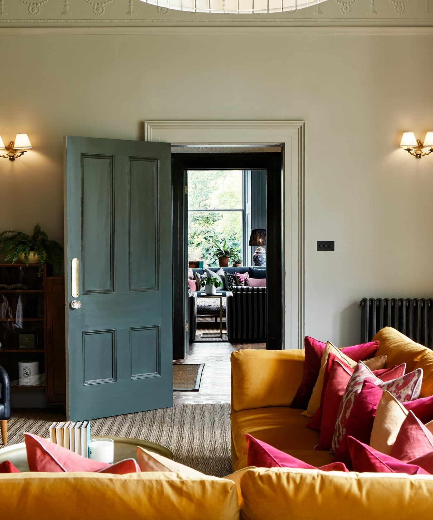 Light green grey living room with yellow sofa, red cushions, and a dark green door.